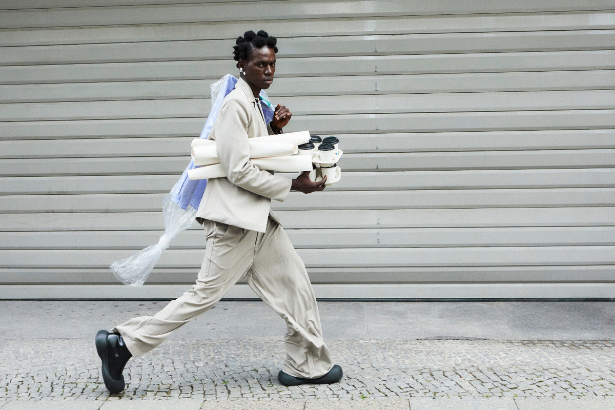 Editorial banner photo of a person walking down a street carrying coffee cups